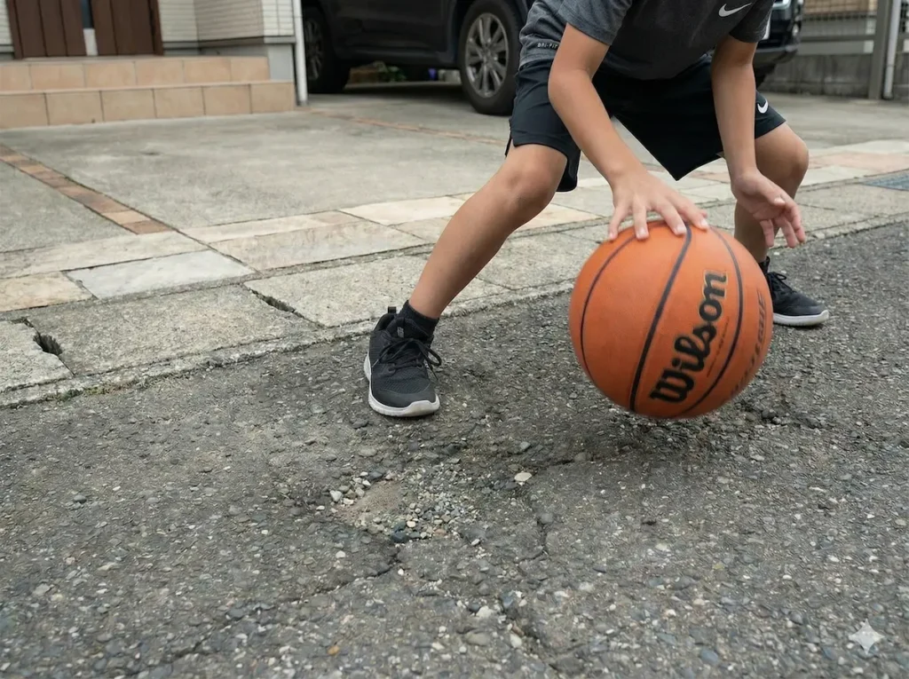 自宅の駐車場のアスファルトでバスケットボールをドリブルする子供の写真。
